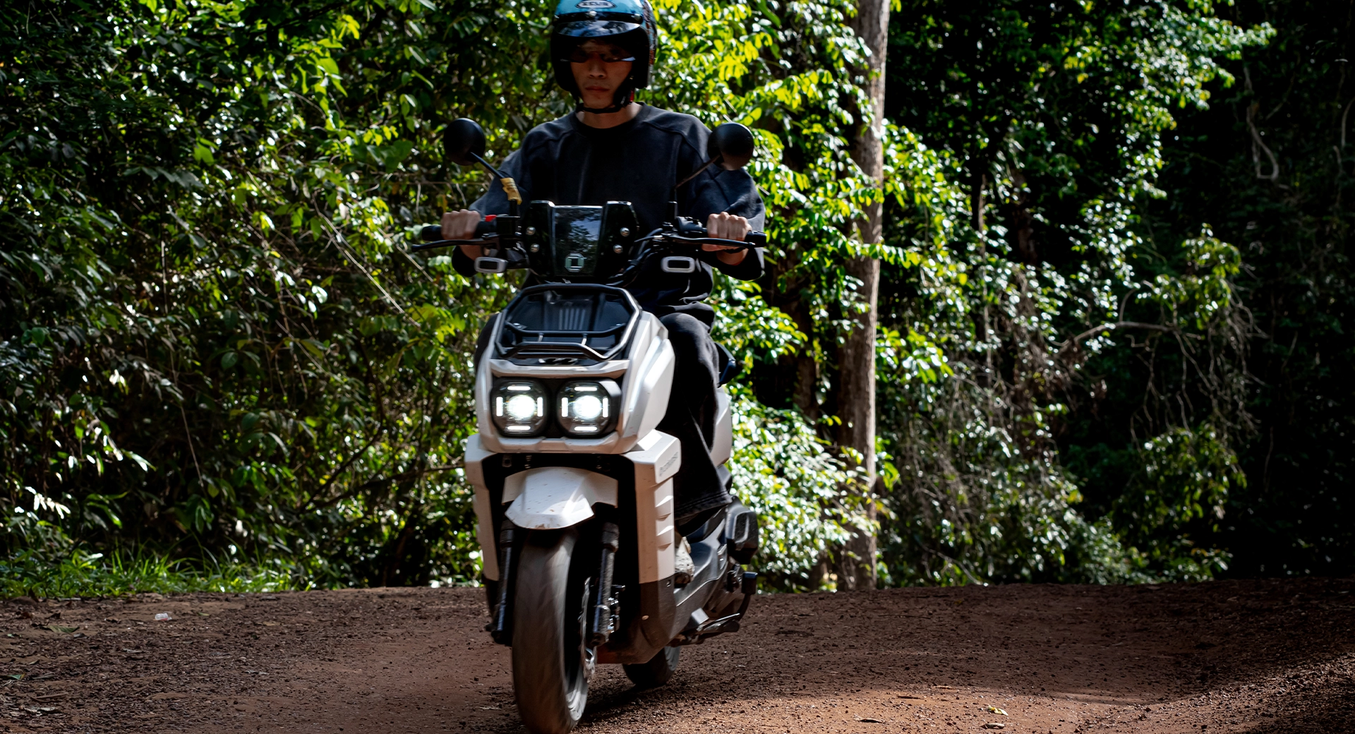 Rider on white Calypso Nijia smart motorcycle on dusty off-road forest trail in Cambodia