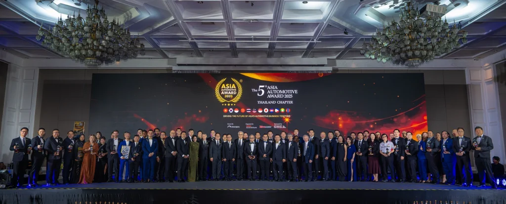 A large group of award recipients and organizers stand on stage at the 5th Asian Automotive Awards 2025, with an LED backdrop displaying the event logo, country flags, and ceremony title.